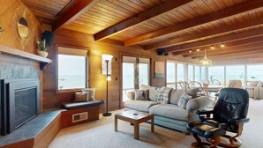 A cozy living room with a fireplace, comfortable seating, and large windows offering a view of the sea. - Oceanfront Haven with Beach Access, Views & Deck (Fort Bragg)