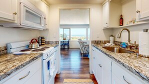 A modern kitchen with white cabinets, granite countertops, a microwave, stove, and a sink. - Ocean View Apartment - Beach Access, Yard, Bikes (Fort Bragg)