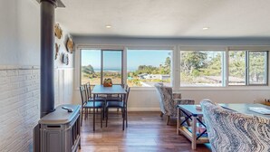 A dining area with a view of the ocean, a fireplace, and a patterned sofa. - Ocean View Apartment - Beach Access, Yard, Bikes (Fort Bragg)