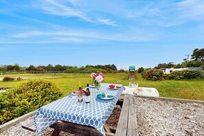 An outdoor dining area with a table set for two, a bottle of wine, and a vase with flowers.