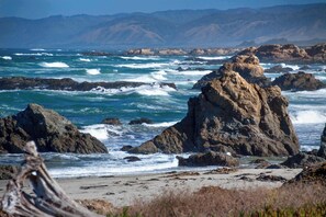 A rocky coastline with waves crashing against large boulders and a sandy beach.