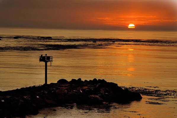 A sunset over a calm sea with a rocky outcrop and a signpost.