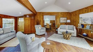 Ein geräumiges Wohnzimmer mit Holzwänden, einem Essbereich und einer durch eine offene Tür sichtbaren Küche.