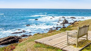 Un banc en bois, installé sur une plateforme surplombant une côte rocheuse où les vagues s’écrasent contre les rochers.