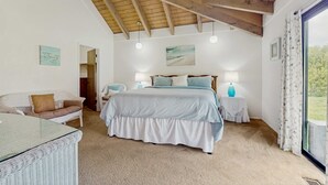 Una camera da letto con un letto grande, un tavolino in vimini bianco, un divano e vista sull'esterno da una finestra.