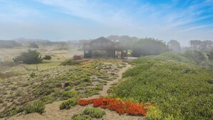 Una casa con un sendero arenoso que la conduce, rodeada de vegetación y un cielo despejado.