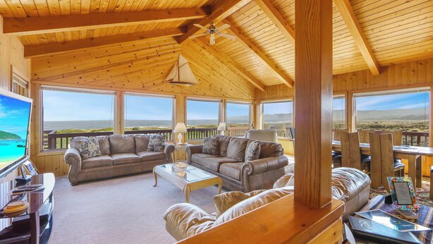 Interior de madera con techo alto, dos sofás, una mesita de centro y vista al océano.