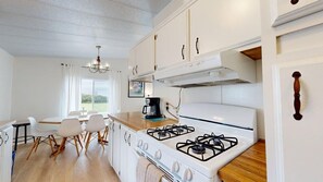 A kitchen with white cabinets, a gas stove, a coffee maker, and a dining area with chairs and a table.