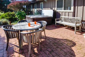 Une terrasse avec une table ronde, quatre chaises, un banc et un jacuzzi.