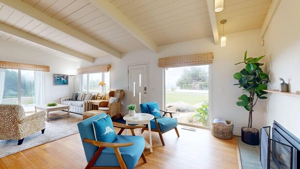 Ein großzügiges Wohnzimmer mit Holzboden, einer Sofagarnitur, einem Couchtisch und einem großen Fenster mit Blick ins Freie.