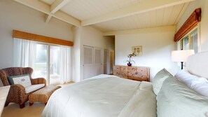 Une chambre à coucher avec un grand lit, une chaise, une commode et une fenêtre avec des rideaux.