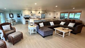 A spacious living area with a sectional sofa, a coffee table, and a dining table. There is a kitchen in the background with white cabinets and a large island. - Oceanfront Haven - Hot Tub & Private Beach Access (Fort Bragg)