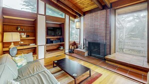 A cozy living room with a fireplace, wooden beams, a sofa, and a TV. - Oceanfront Blufftop Home - Wide Deck & Water Views (Elk)