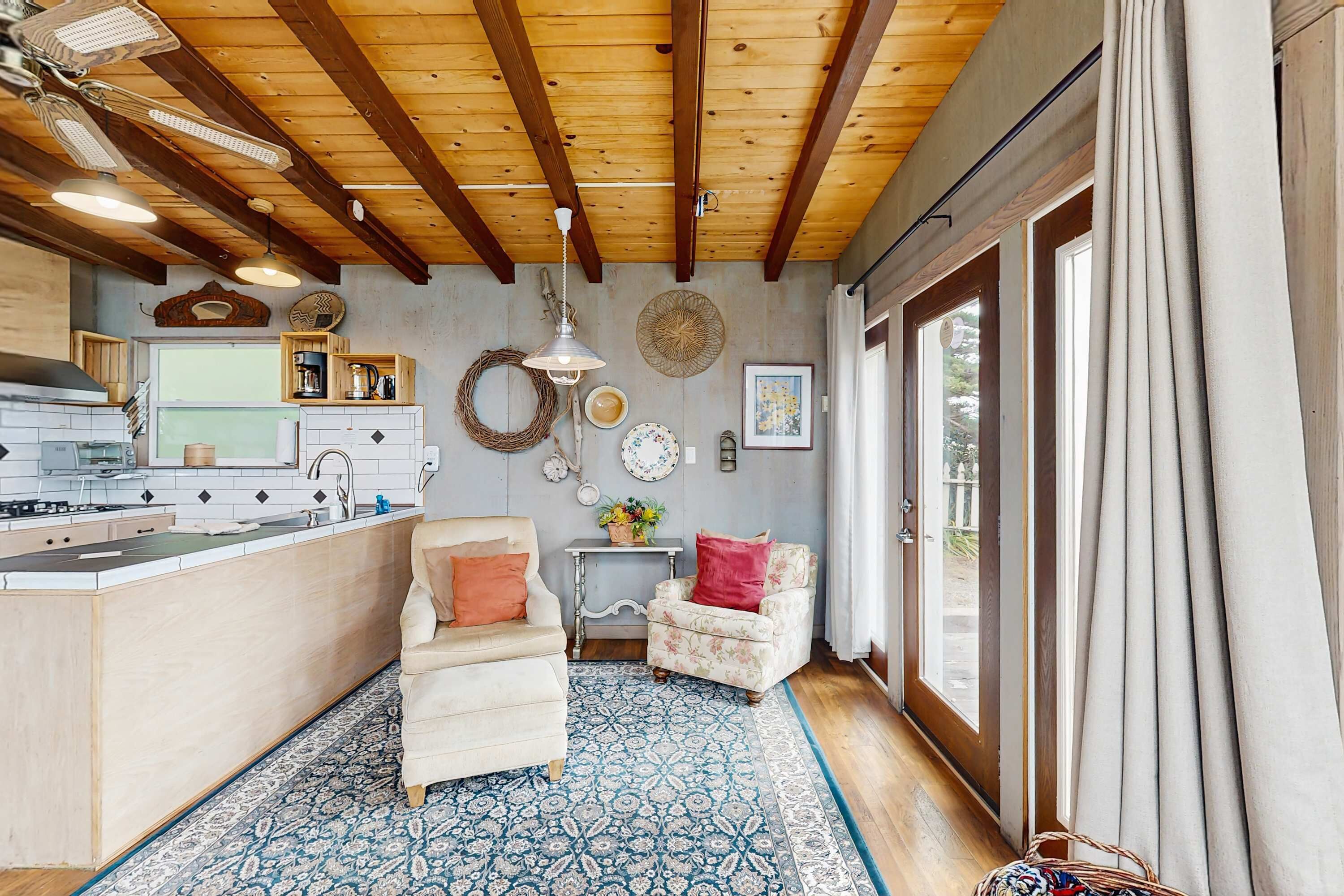 A cozy kitchen with a dining area, wooden ceiling beams, and a large window with curtains.