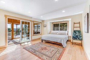 A bedroom with a large bed, a wooden floor, a window, and a view of the outdoors. - Stunning 3BR with ridge top views and hot tub (Little River)