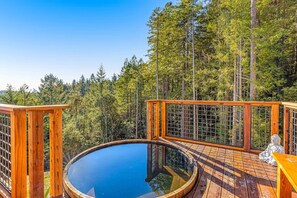 A wooden deck with a circular hot tub, surrounded by a forest. - Stunning 3BR with ridge top views and hot tub (Little River)