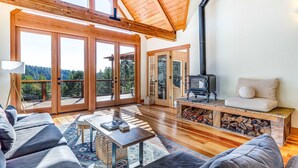 Amplia sala de estar con techo de madera, chimenea, sofá y un gran ventanal corredero que da a una terraza exterior.