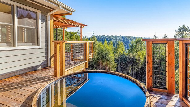Una terraza de madera con piscina, con vista a un área boscosa.