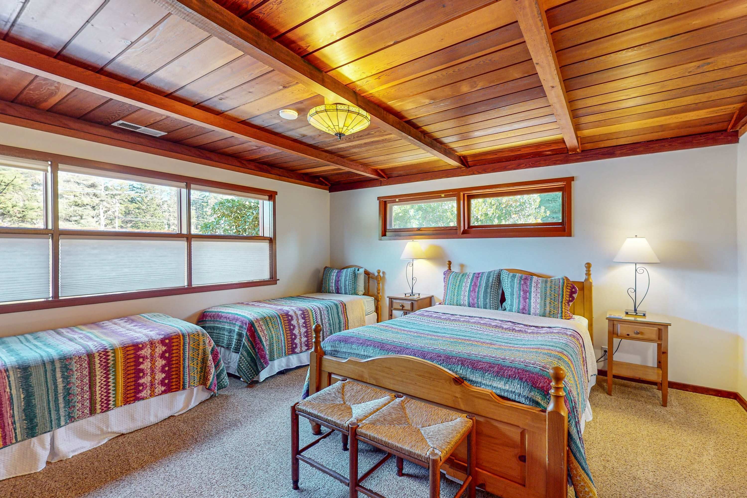A bedroom with two single beds, a wooden bench, and a large window.