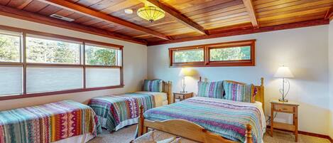 A bedroom with two single beds, a wooden bench, and a large window.