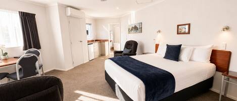 Habitación de hotel con cama, escritorio, silla, ventilador de techo y obras de arte en las paredes.