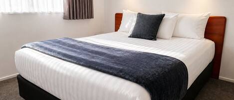 A neatly made bed with a dark blue blanket, white pillows, and a wooden headboard.
