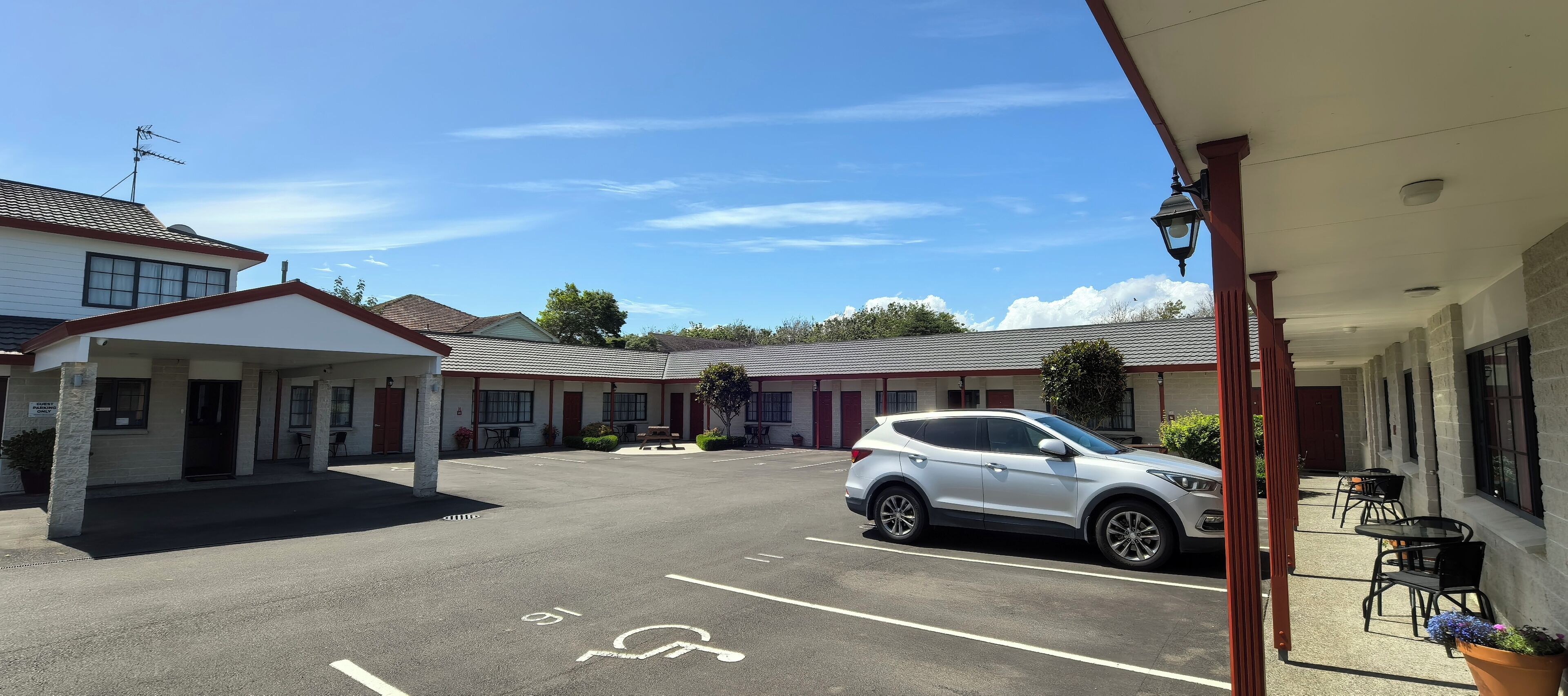 A motel with a parking lot, a white SUV parked, and a covered outdoor seating area.