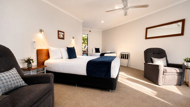 Une chambre à coucher comprenant un lit, une chaise, un bureau, un ventilateur de plafond et une fenêtre.