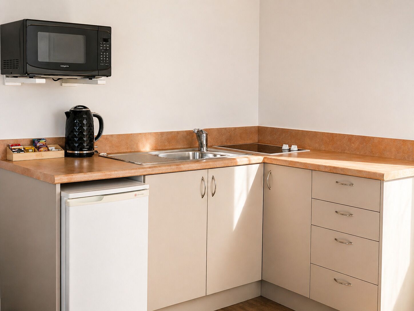 Una cocina compacta equipada con microondas, hervidor, lavabo y lavavajillas.