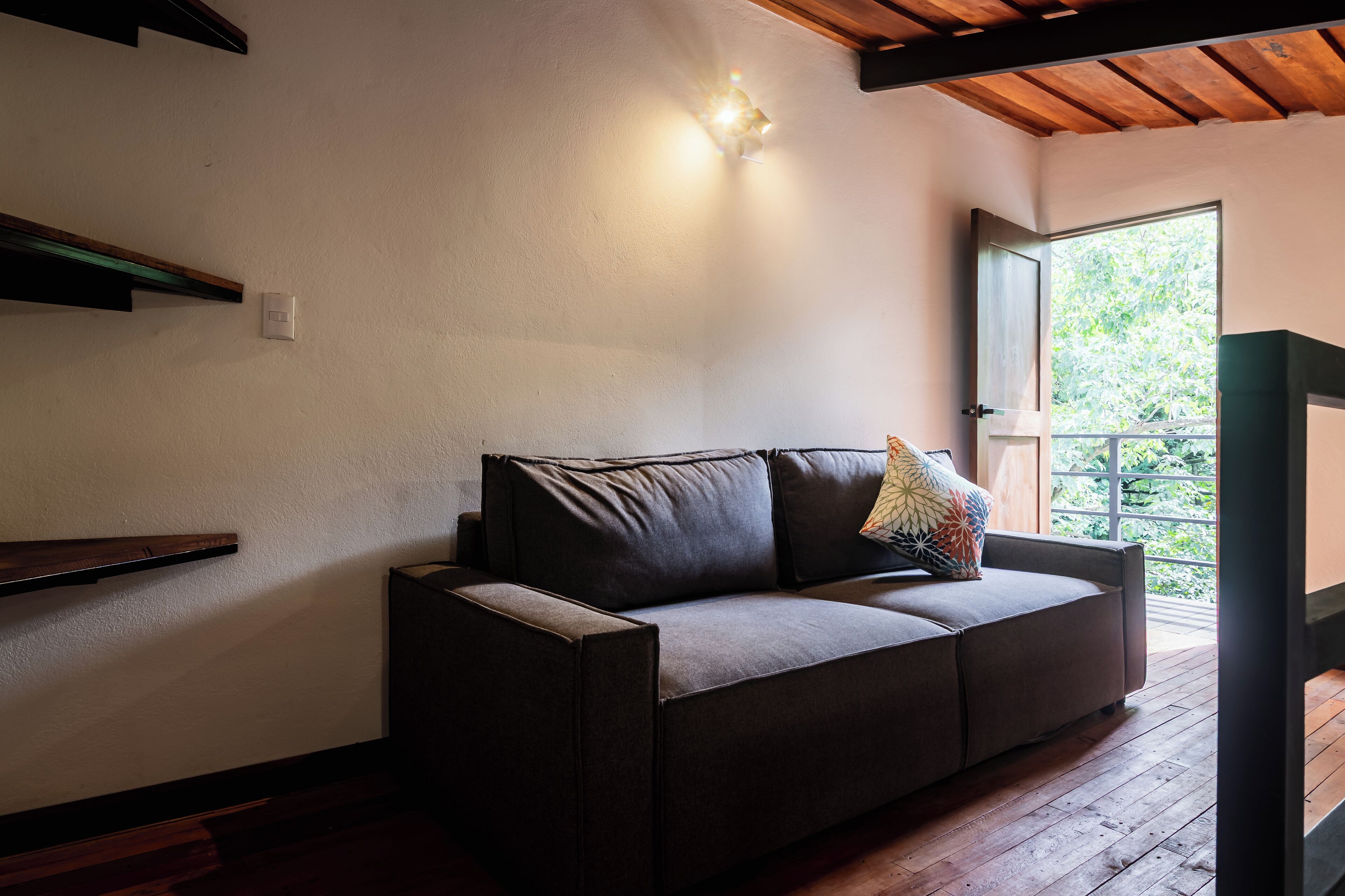 Una habitación acogedora con un sofá marrón oscuro, techo de madera y ventana con vistas a la vegetación.