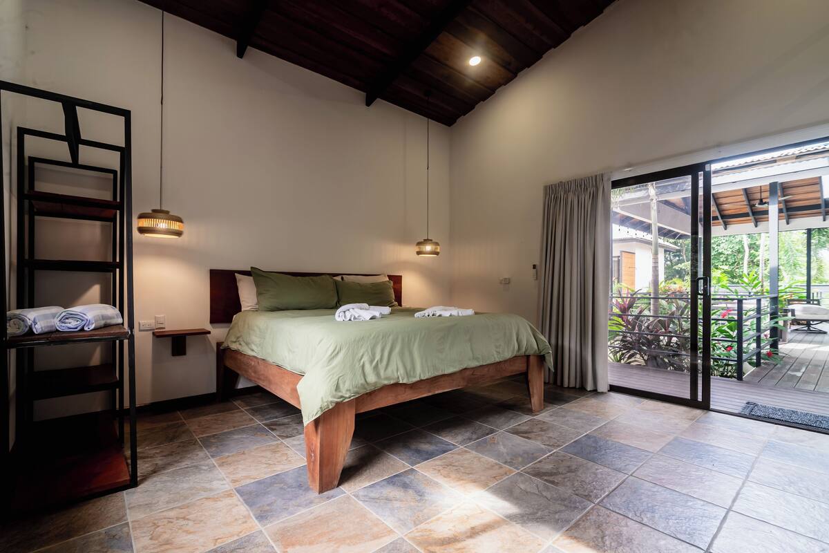 Un dormitorio con una cama de madera, una repisa con toallas y vistas al exterior a través de un ventanal.