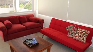 Ein Wohnzimmer mit zwei roten Sofas, einem Holztisch und einem großen Fenster mit Blick auf eine Brücke und Bäume.