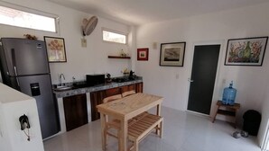 Eine kompakte Küche mit Kühlschrank, Herd und Spüle. Es gibt einen Holztisch mit Bänken, einen Wasserspender und eine Tür mit einem Bild.