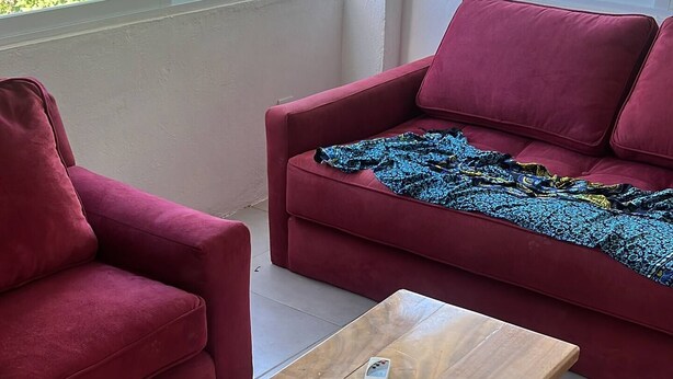 Ein modernes Wohnzimmer mit einem roten Sofa, einem passenden Sessel und einem Holztisch mit einer Fernbedienung darauf.