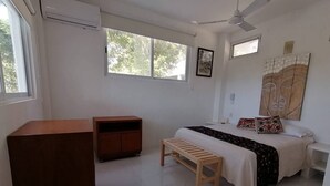 Ein Schlafzimmer mit einem Bett, einer hölzernen Bank, einer kleinen Kommode und einem Deckenventilator.
