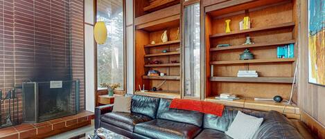 A cozy living room with a leather sofa, wooden shelves, and a fireplace.