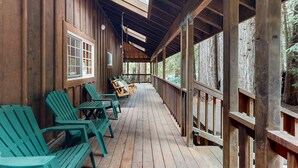 Une terrasse en bois avec des fauteuils Adirondack verts, une rambarde en bois et une lucarne.