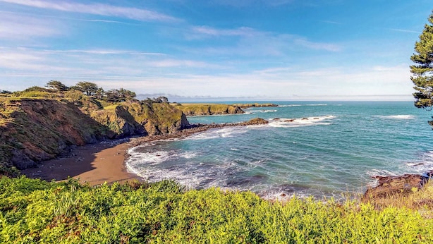 Un paisaje costero con acantilados rocosos, una playa de arena y el océano.