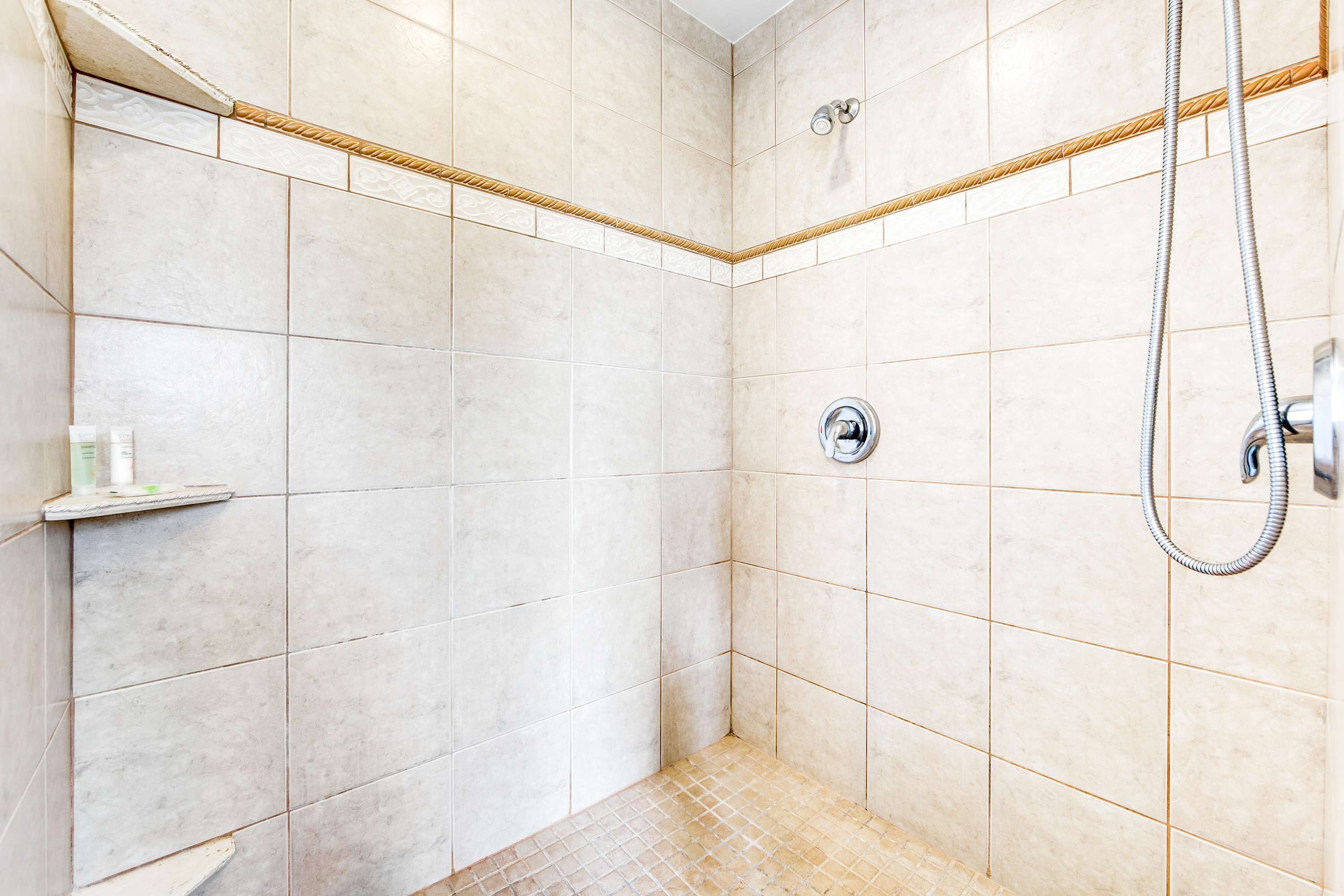 A small, tiled shower area with a showerhead and a shelf with toiletries.