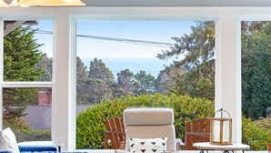 A room with a view of the ocean, a chair, a table, and a lamp.