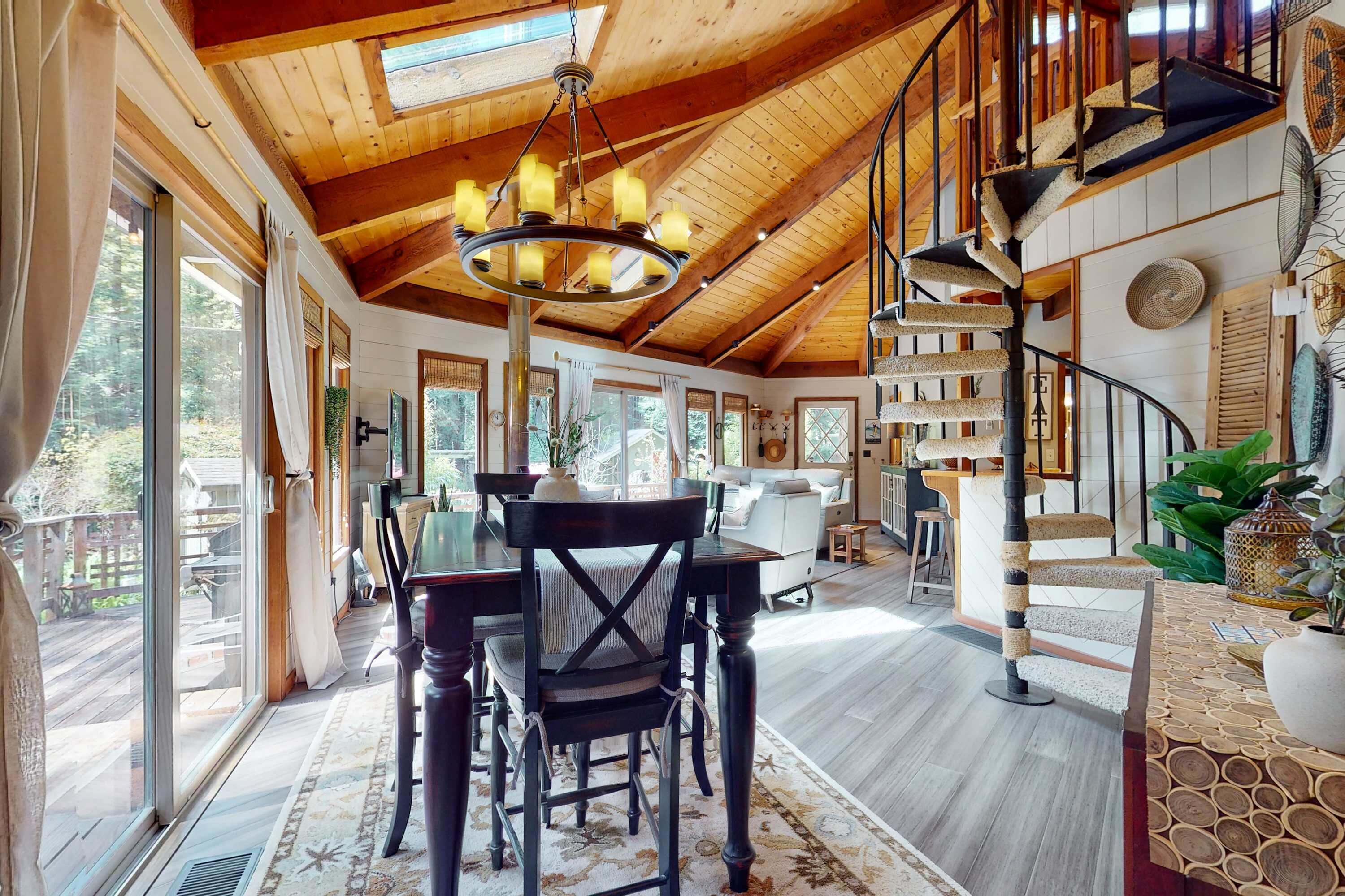 Une pièce spacieuse avec un plafond haut, des poutres apparentes, un escalier en colimaçon et un coin repas comprenant une table et des chaises.