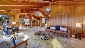 A spacious living room with wooden paneling, a large coffee table, and a sofa. - Luxe Remodeled Oceanfront Home on the Bluff (Mendocino)
