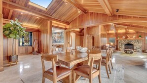 A spacious wooden interior with a large dining table, chairs, and a stone fireplace. - Luxe Remodeled Oceanfront Home on the Bluff (Mendocino)