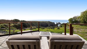 A wooden deck with two cushioned chairs facing a scenic ocean view. - Luxe Remodeled Oceanfront Home on the Bluff (Mendocino)
