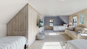 Una camera da letto con soffitto spiovente, pareti in legno, un'ampia finestra, un letto, un divano e una televisione.