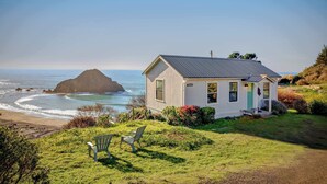 Una casa costera con vista al océano y una gran formación rocosa.