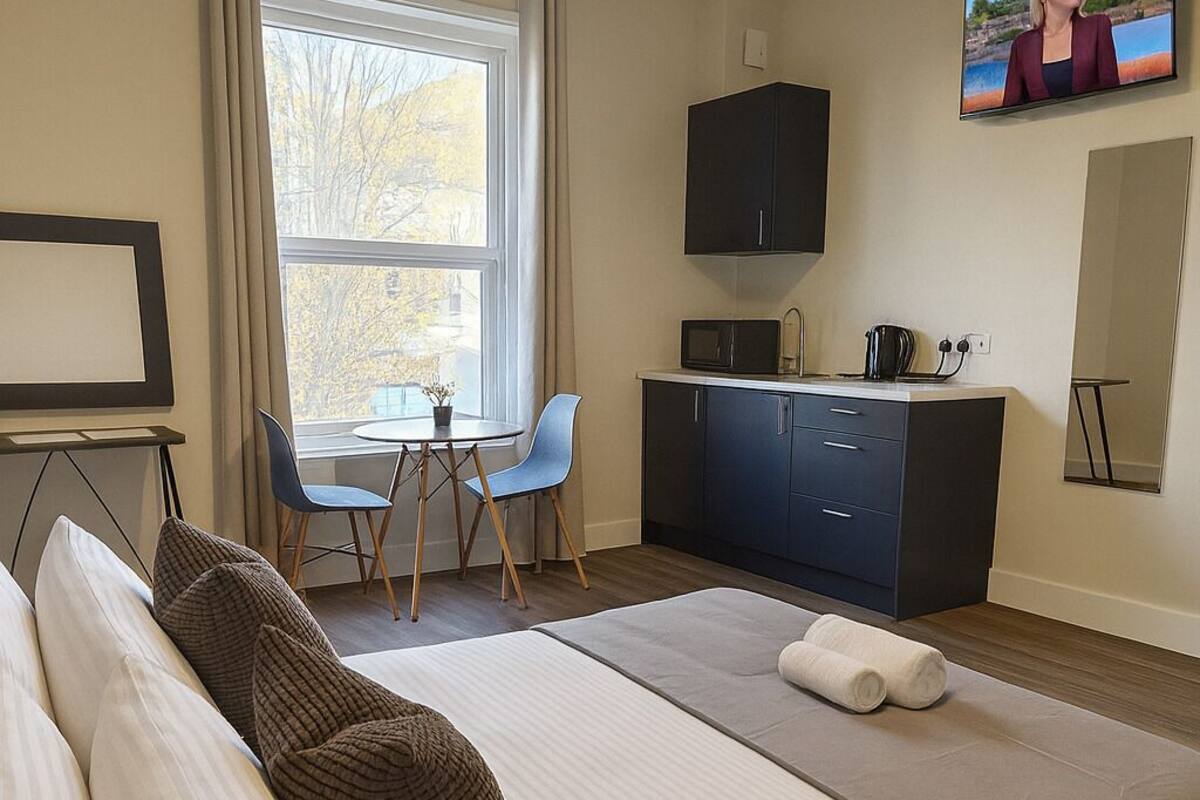 A hotel room with a bed, a desk, a chair, a TV, and a window.