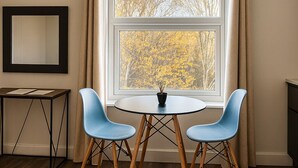 A room with a large window, a round table with two chairs, a small table with papers, and a mirror on the wall. - City Stays Norwich (Norwich)