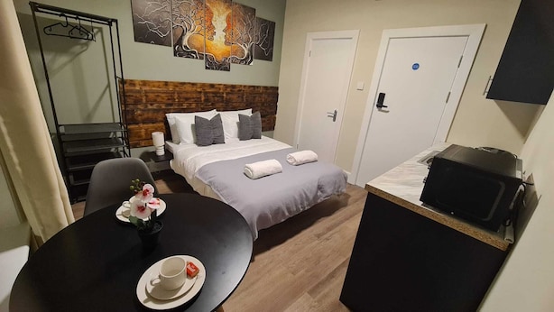 A hotel room with a bed, a desk with a chair, a table with a cup and saucer, and a TV on a cabinet. - City Stays Norwich (Norwich)