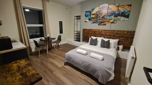 A hotel room with a bed, a desk with chairs, a window, and a painting on the wall. - City Stays Norwich (Norwich)